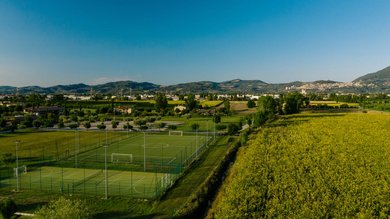 Resort Hotel Assisi com Padel Tennis Bike Hotel 3 swimming pools soccer field. Green sports fields next to yellow fields and hills under blue sky