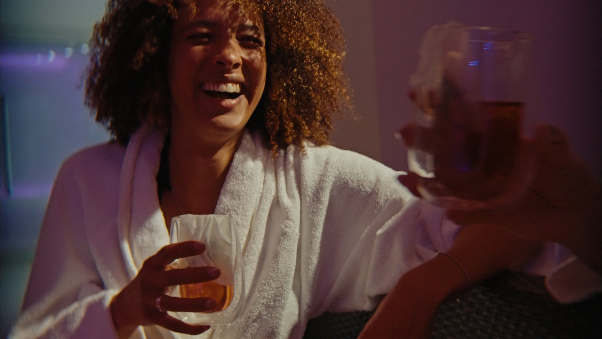 A day dedicated to wellness Woman in white bathrobe laughing and holding a glass with drink