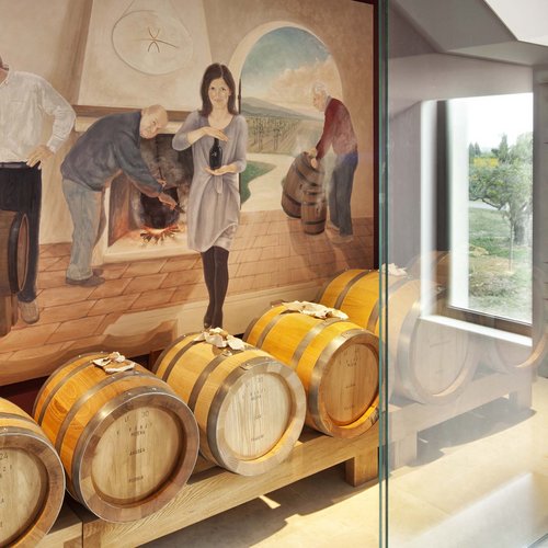 La missione di Valle di Assisi Barili di legno per balsamico davanti a murale in cantina