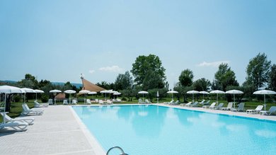 Resort Hotel Assisi com Padel Tennis Bike Hotel 3 swimming pools soccer field. Empty outdoor pool with white loungers and umbrellas in a green park