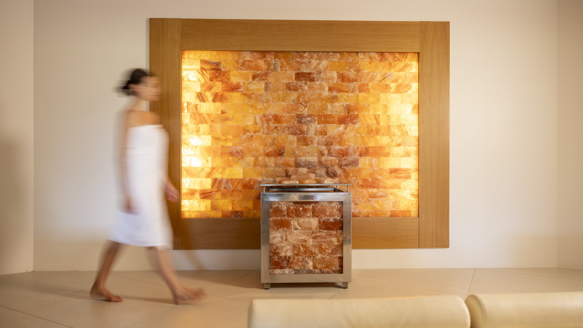 A day dedicated to wellness Woman in white towel walking past a glowing pink salt wall